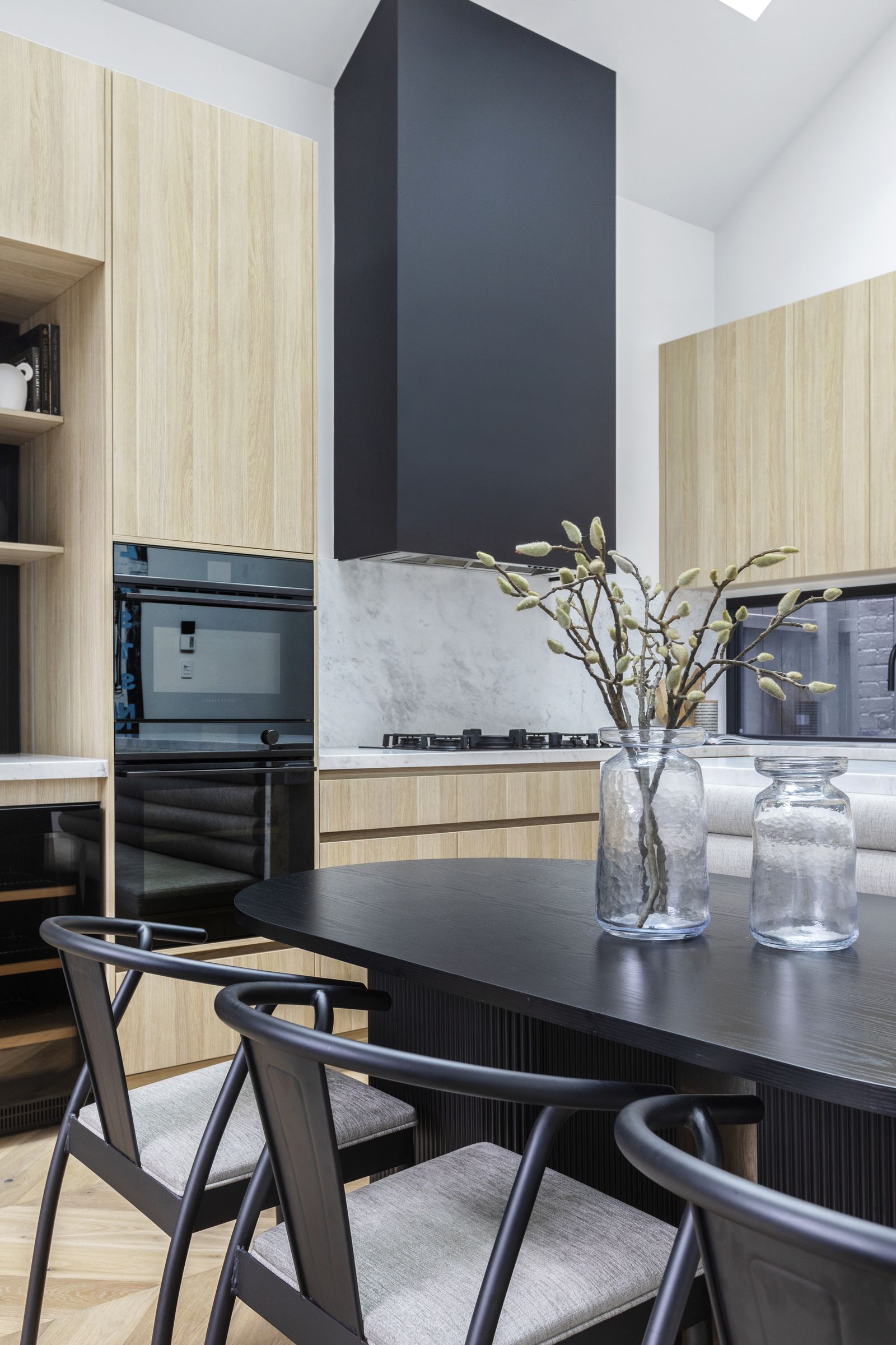 Black dining chairs at a fluted pedestal table in front of the kitchen