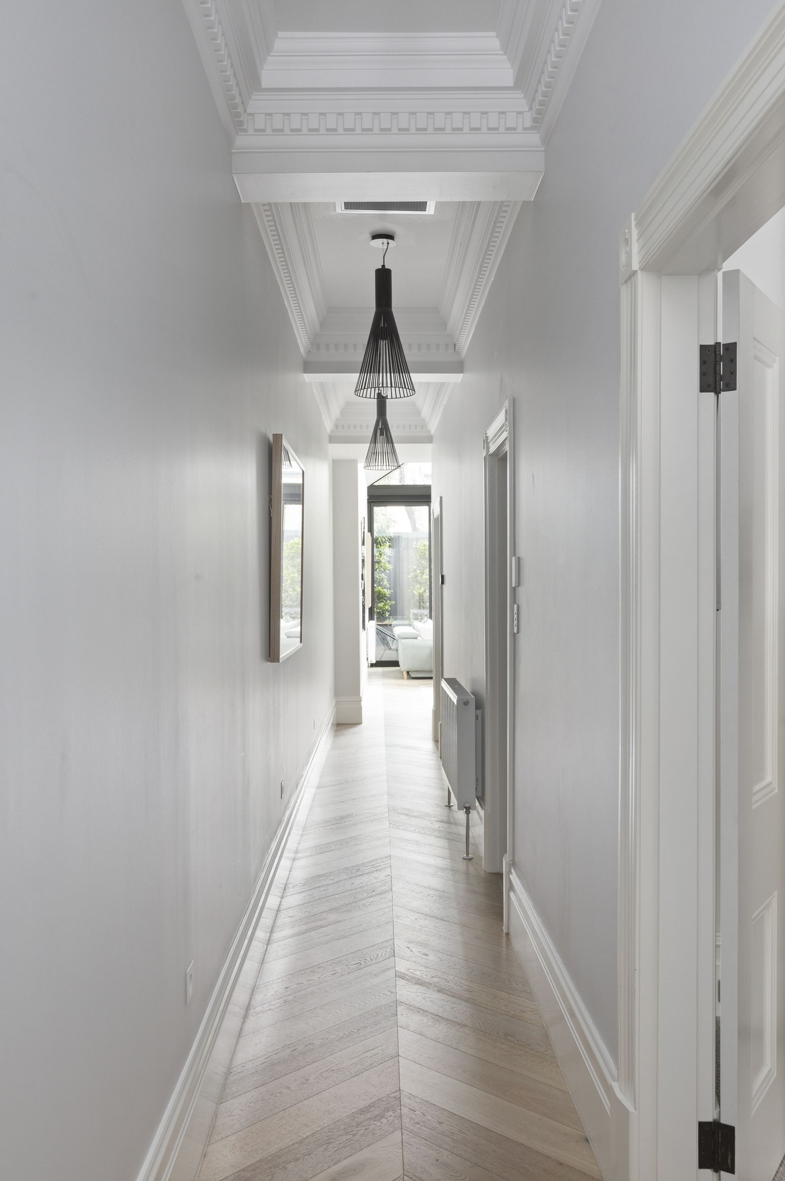 Long hallway with dentil cornices, black pendant lights and chevron oak floors leading to the rear