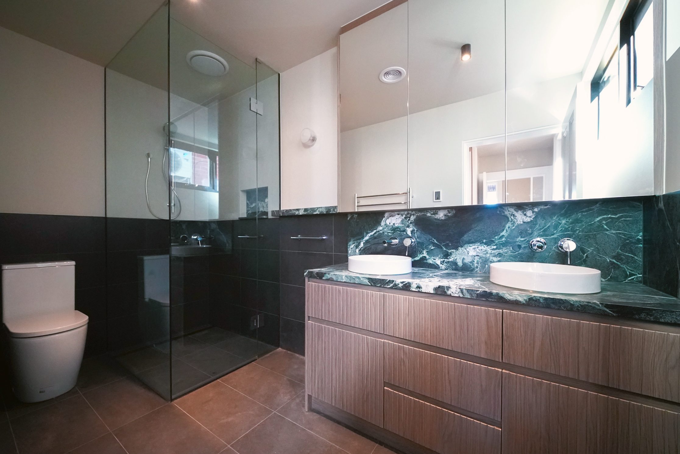 Ensuite with a green marble benchtop and splashback, twin basins and fluted timber vanity