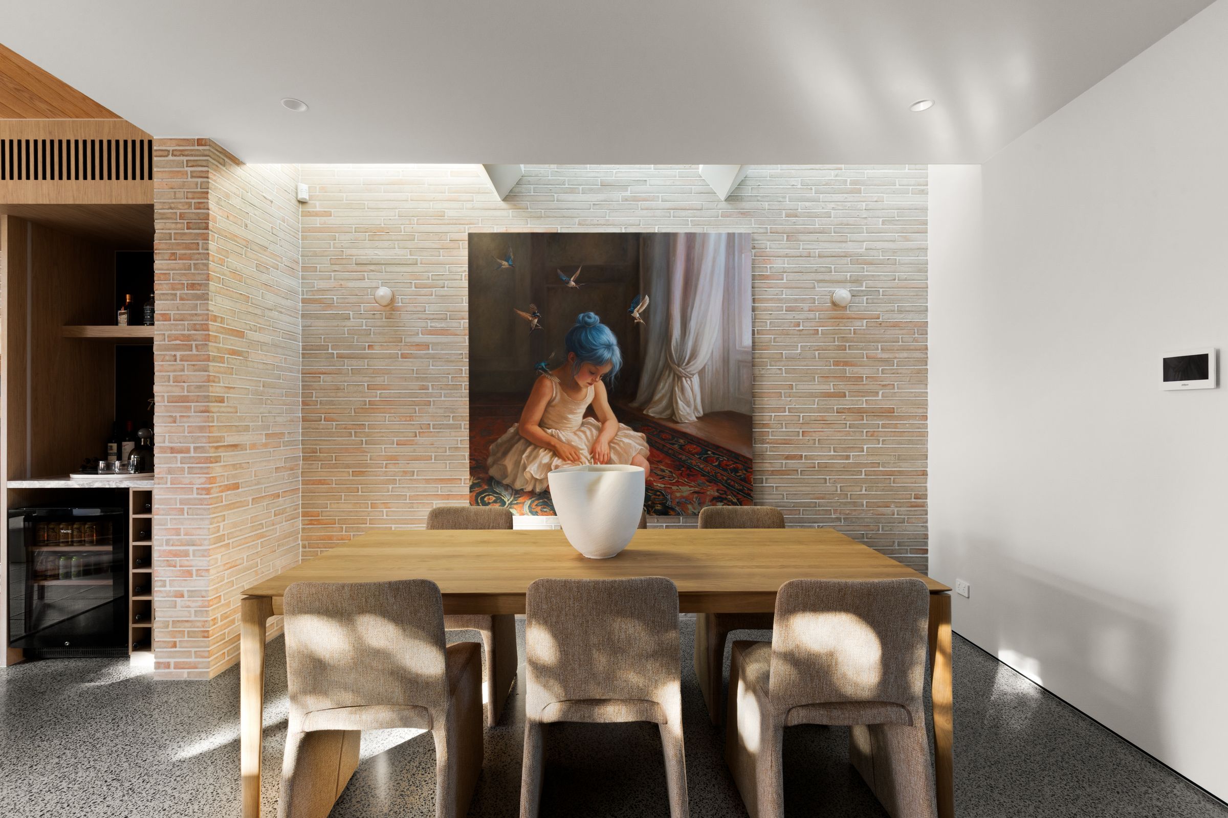 Dining table set against a skylit brick wall with a large portrait painting