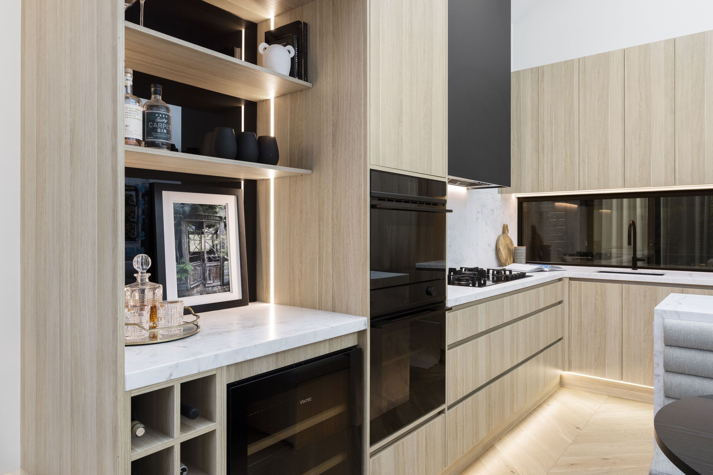 Kitchen with a tall black rangehood, marble splashback and oak cabinetry around a marble island