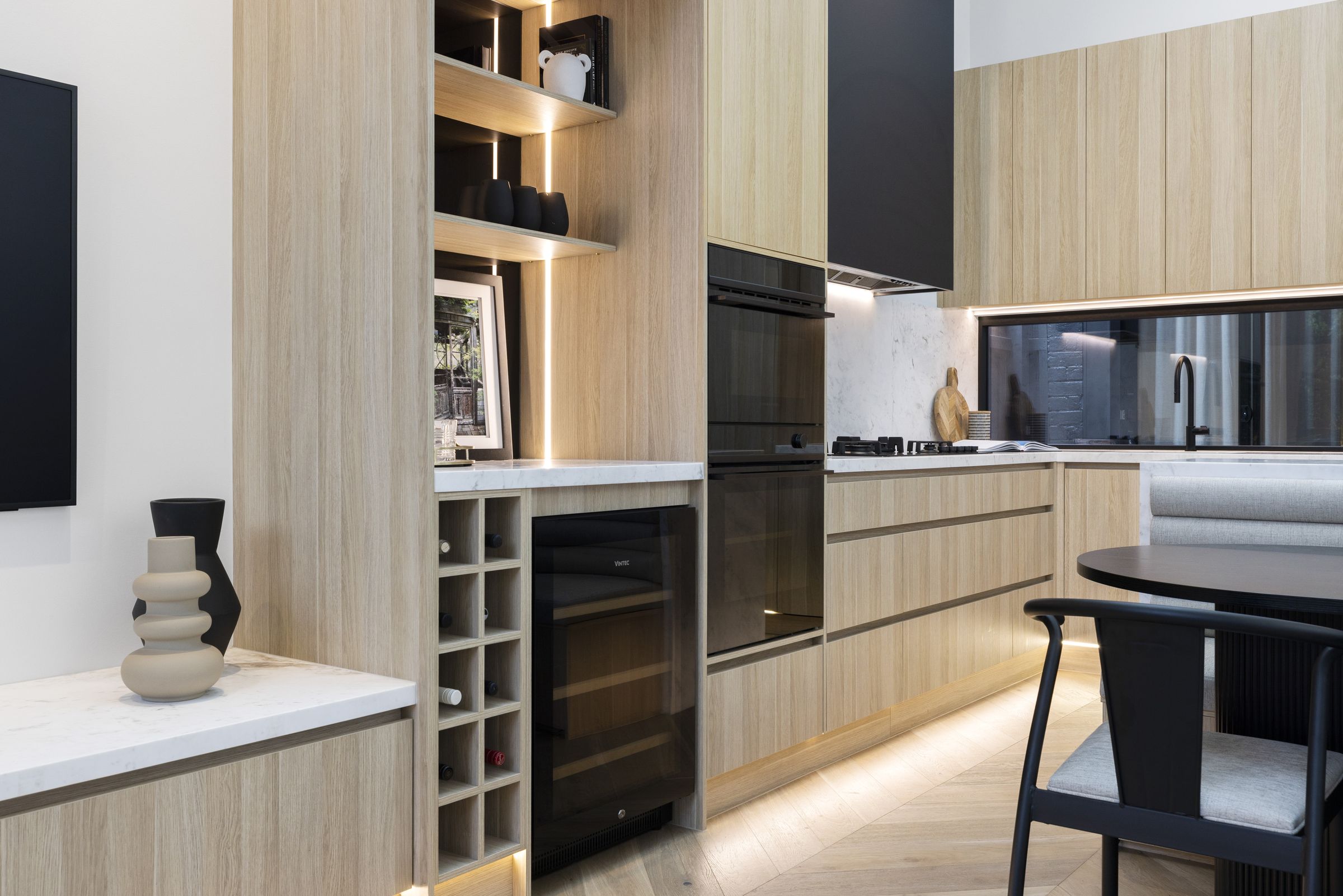 Oak bar joinery with lit shelving, wine storage and integrated ovens leading to the kitchen