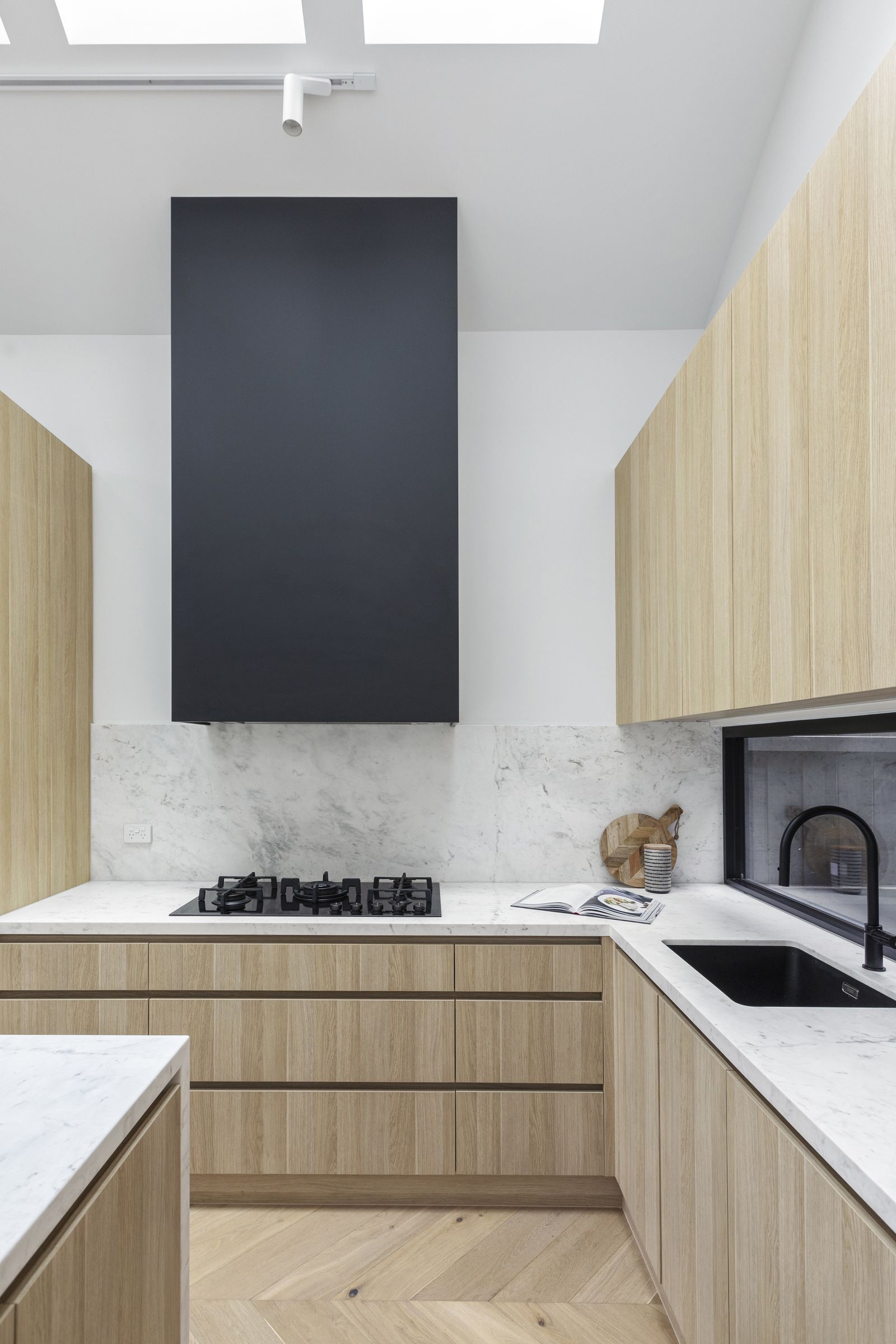 Kitchen with a tall black rangehood, marble splashback and oak cabinetry