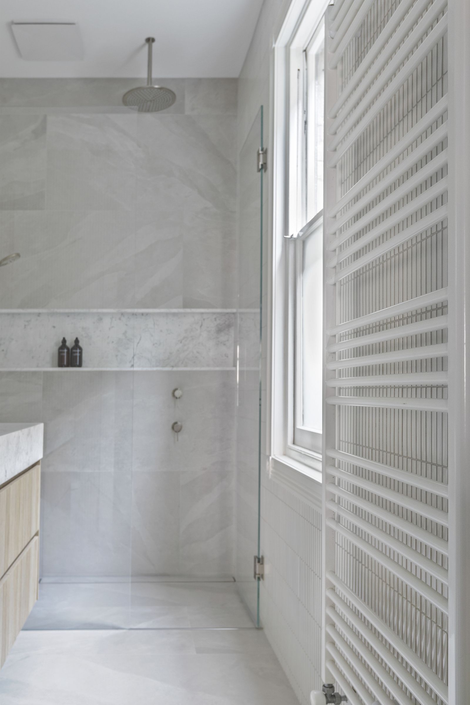 Walk-in shower with large-format stone-look tiles, marble niche and heated towel rail