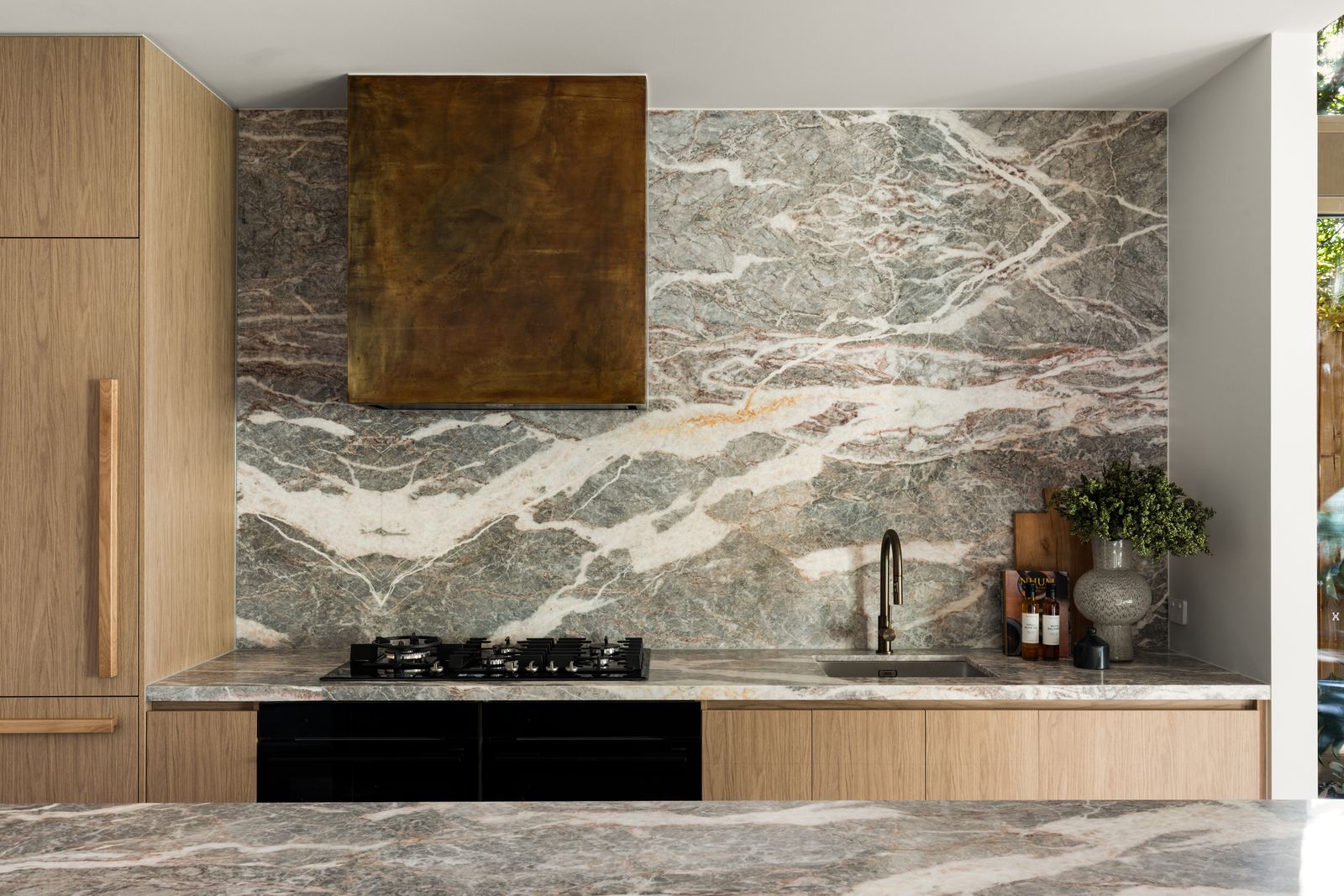 Kitchen elevation with a veined marble splashback and aged brass rangehood