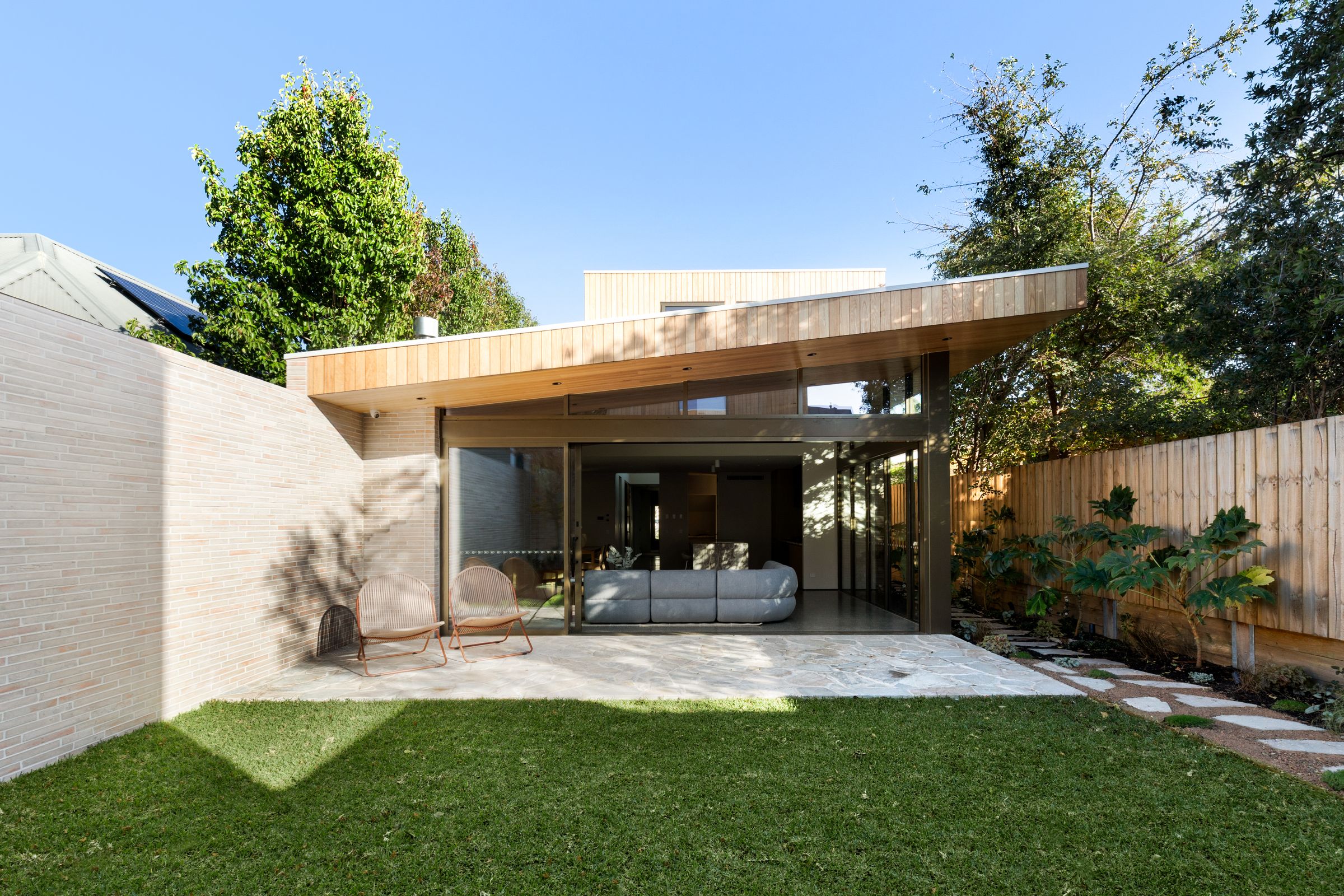 Rear pavilion with a timber-lined skillion roof opening onto a stone terrace and lawn