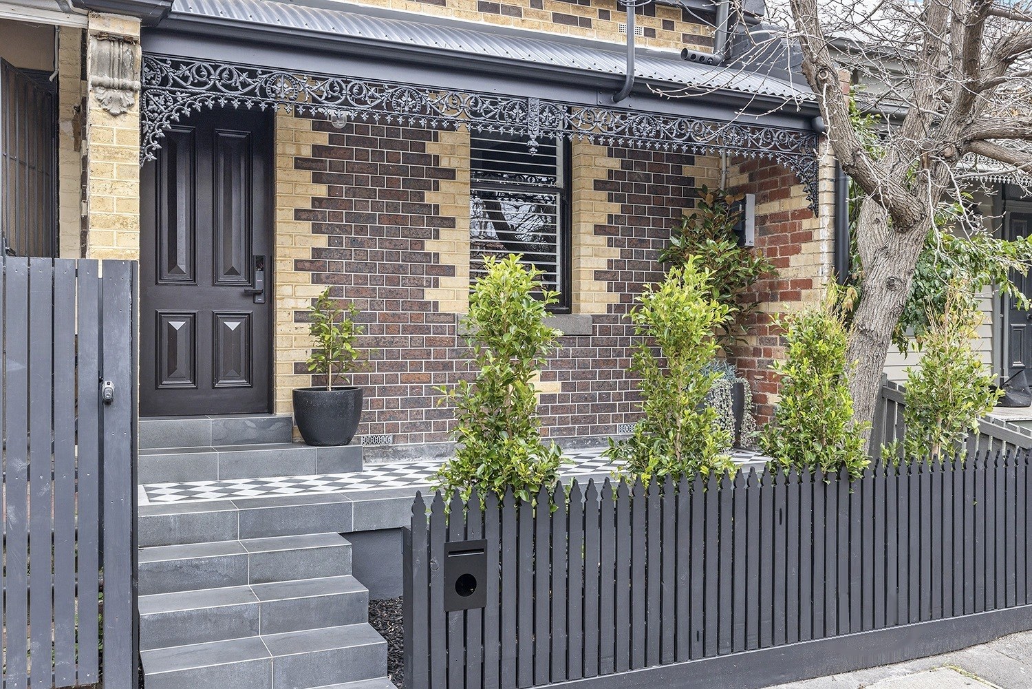 Henry from the street: a Hawthorn brick Victorian with cast-iron lacework and a charcoal picket fence
