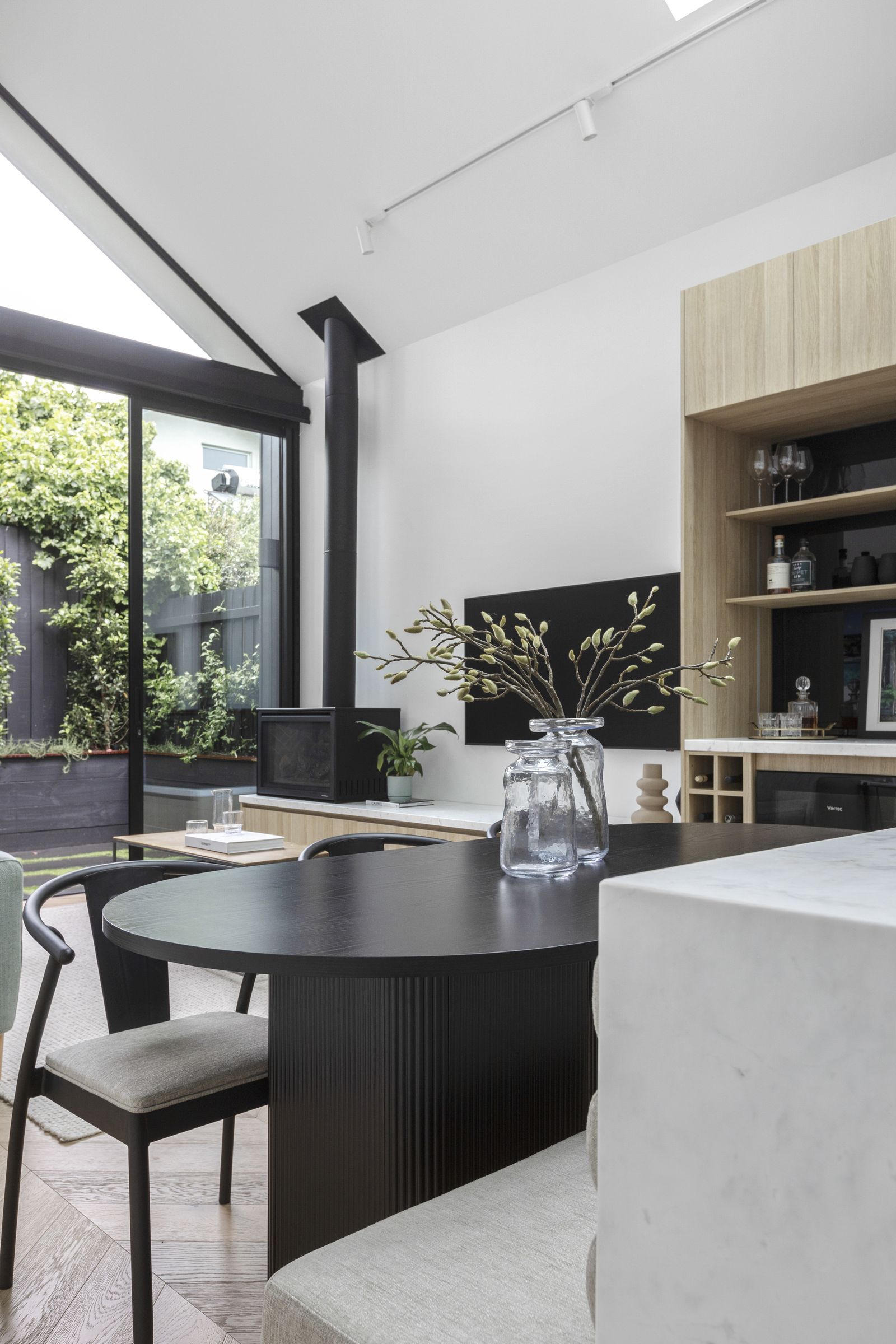 Dining table looking out through sliding doors to a planted courtyard, with a freestanding fireplace