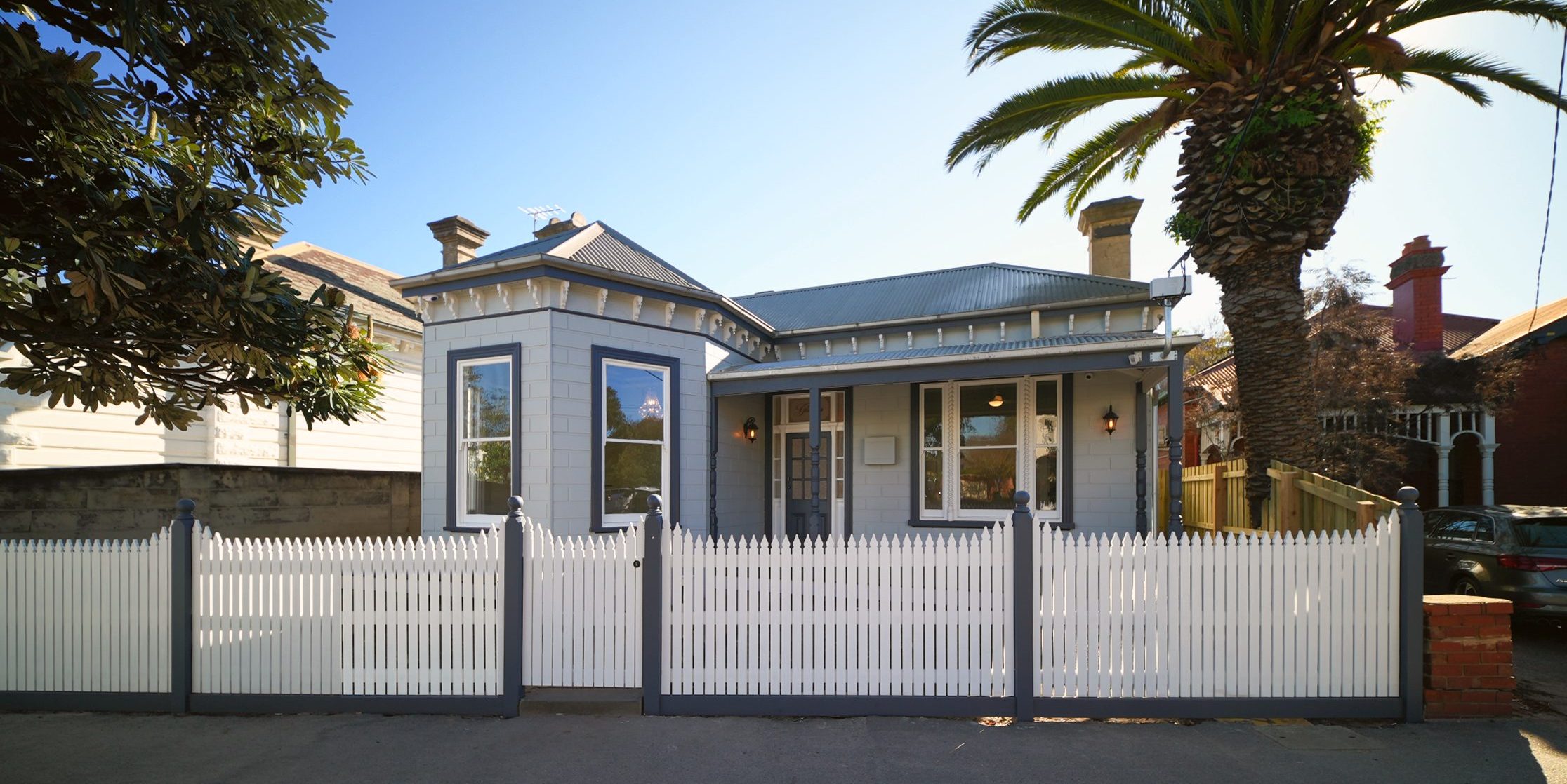 Glenara from the street: a restored Victorian villa behind a white picket fence, framed by a palm
