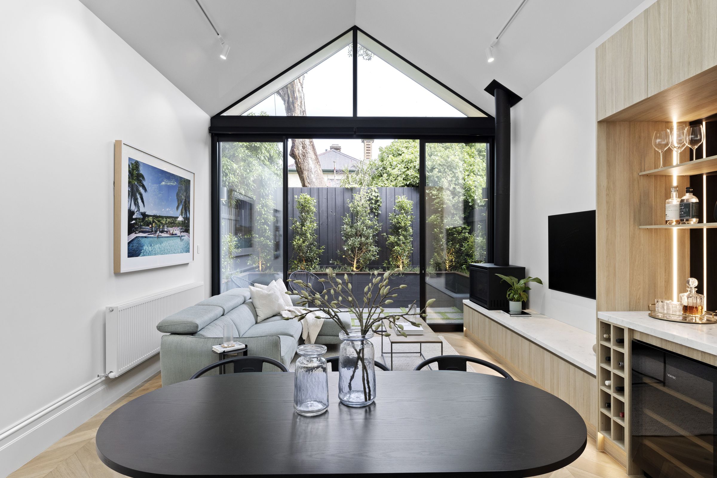 Living and dining under a vaulted ceiling, with a full-height gable window and sliding doors to the courtyard