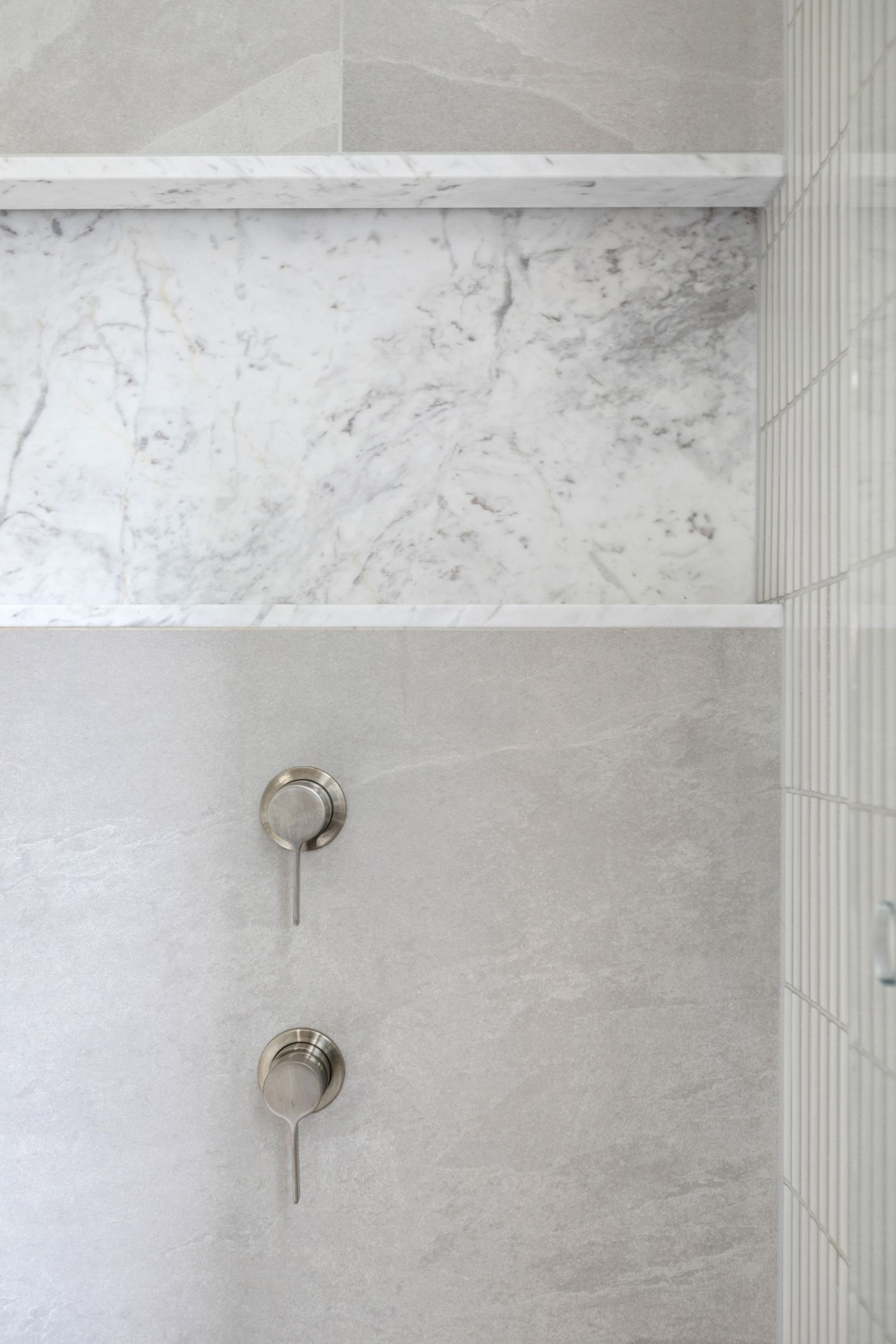Shower mixers below a marble niche set into stone-look tiles