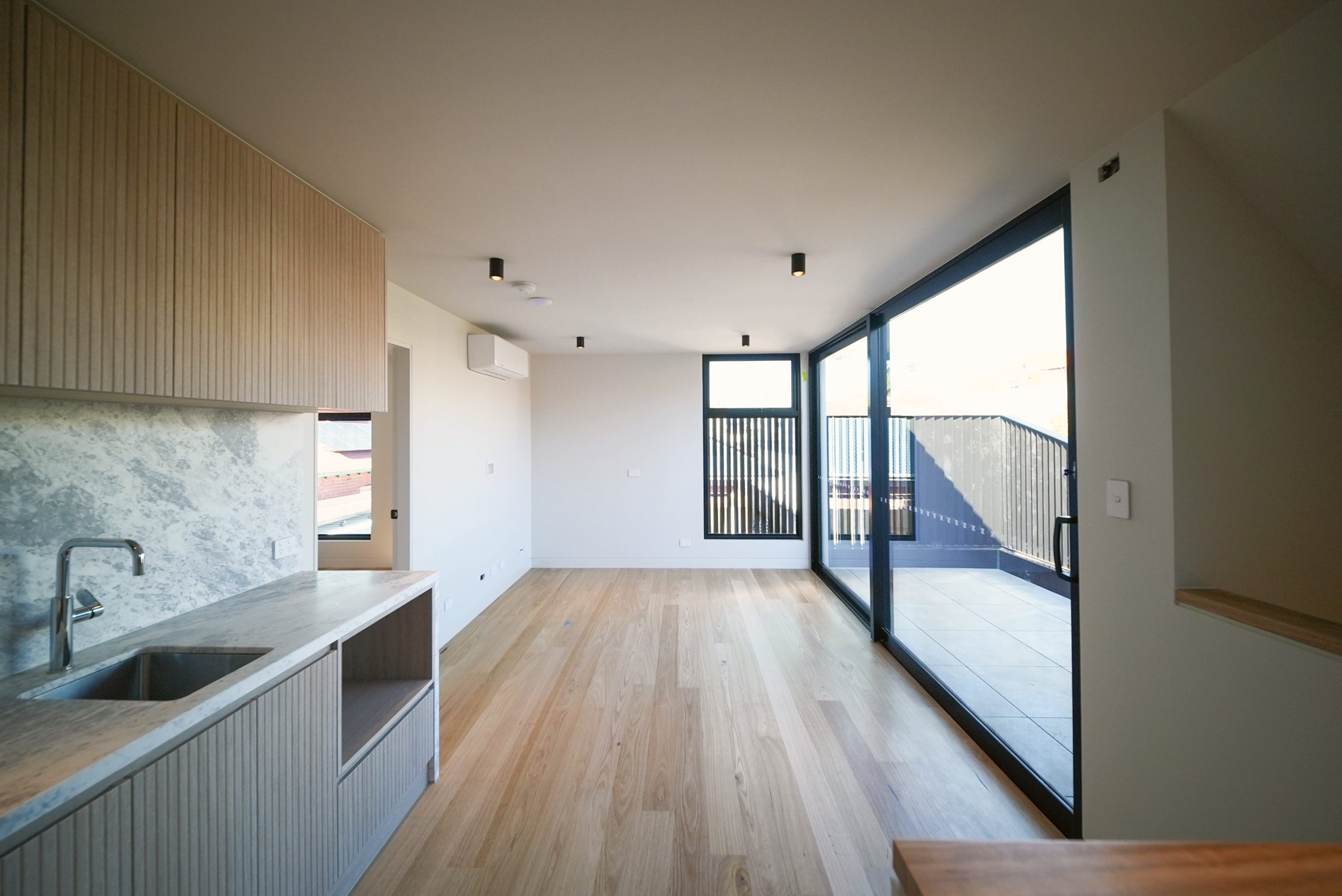 Upstairs living space with a fluted timber kitchenette, stone splashback and sliding doors to a terrace