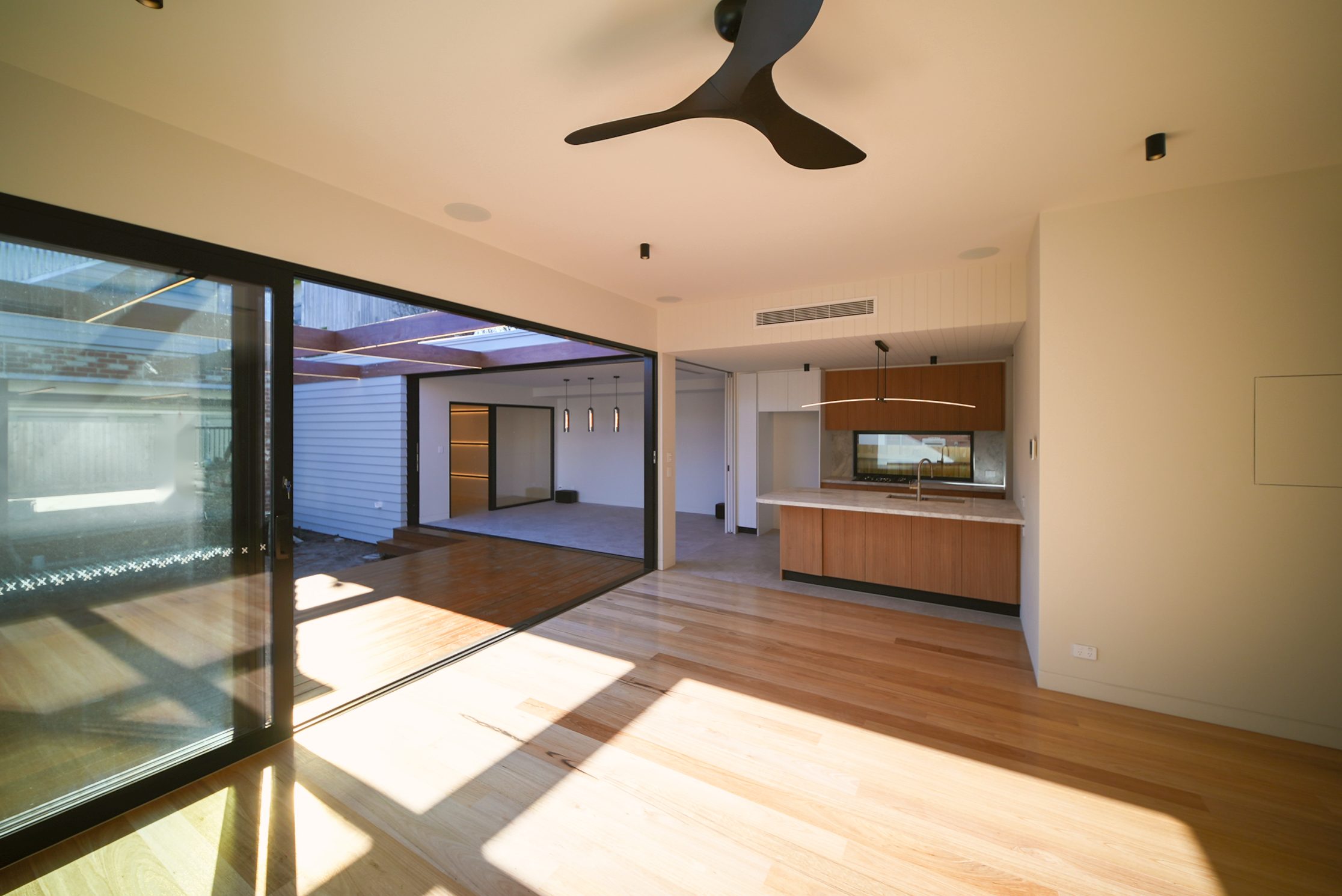 Sunlit living room with a black ceiling fan, sliding doors to the deck and the kitchen beyond