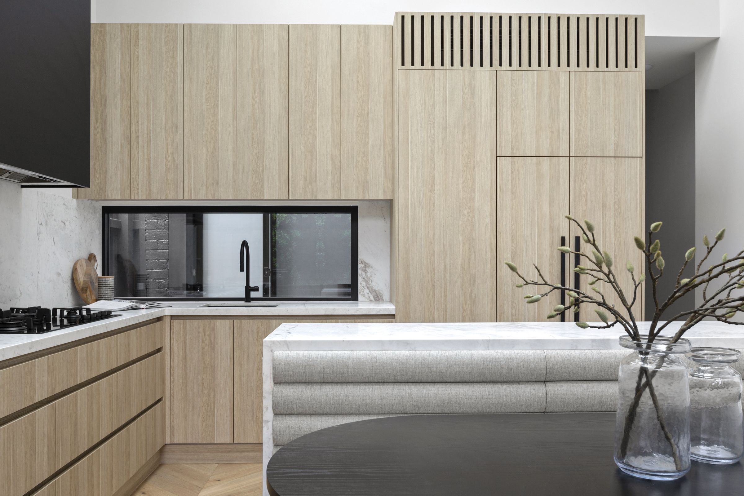 Oak kitchen joinery with a marble benchtop, slot window to a courtyard and a black rangehood