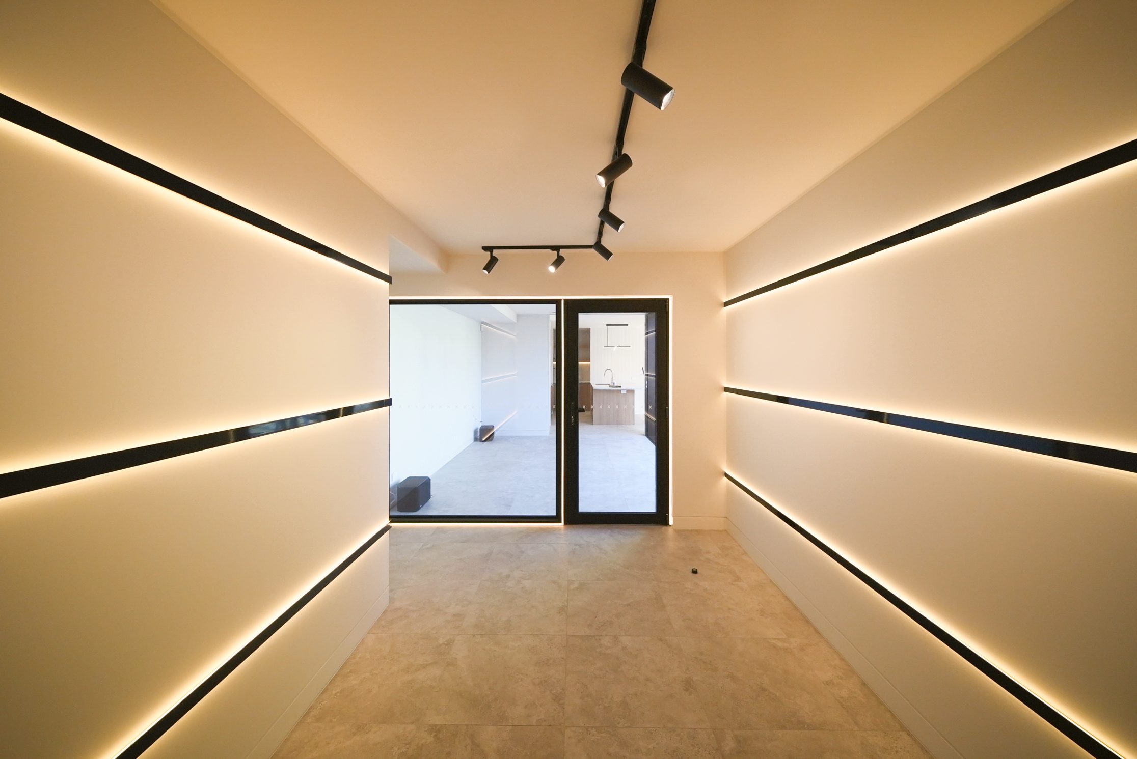 Gallery room with recessed linear lighting and track spotlights, looking through glazing to the rumpus room