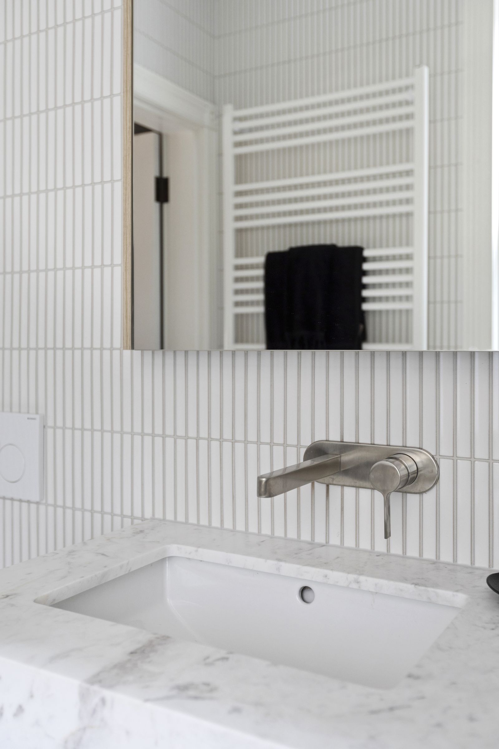 Brushed nickel wall tap above a marble vanity and finger-tiled wall