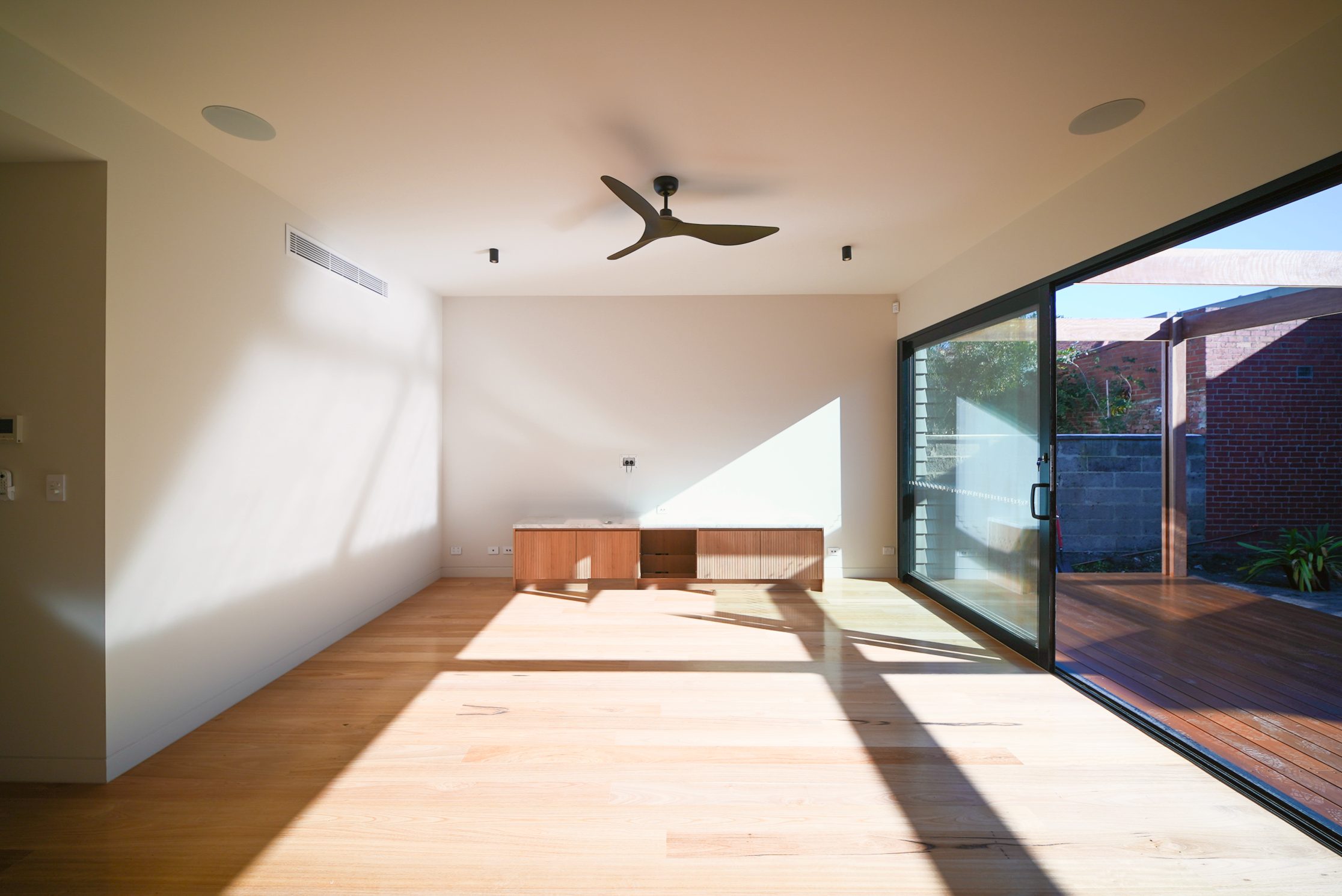 Living room with a fluted timber media unit and full-height sliding doors to the courtyard