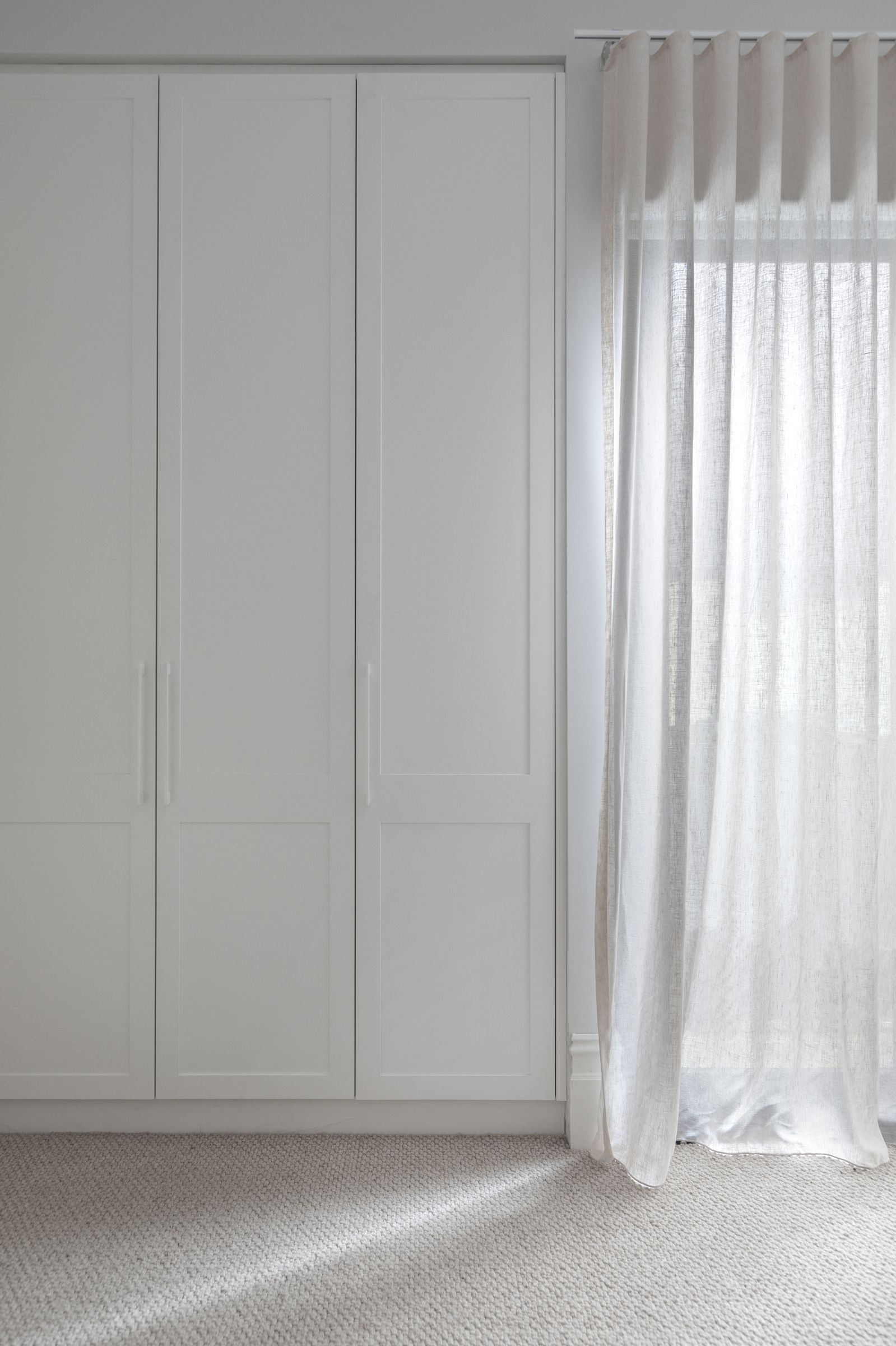 Built-in shaker-style wardrobe beside sheer linen curtains