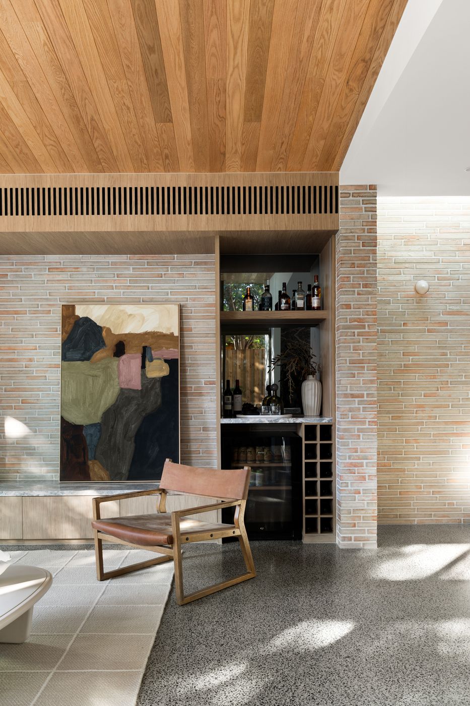 Oak bar joinery set into the brick wall beside a leather armchair