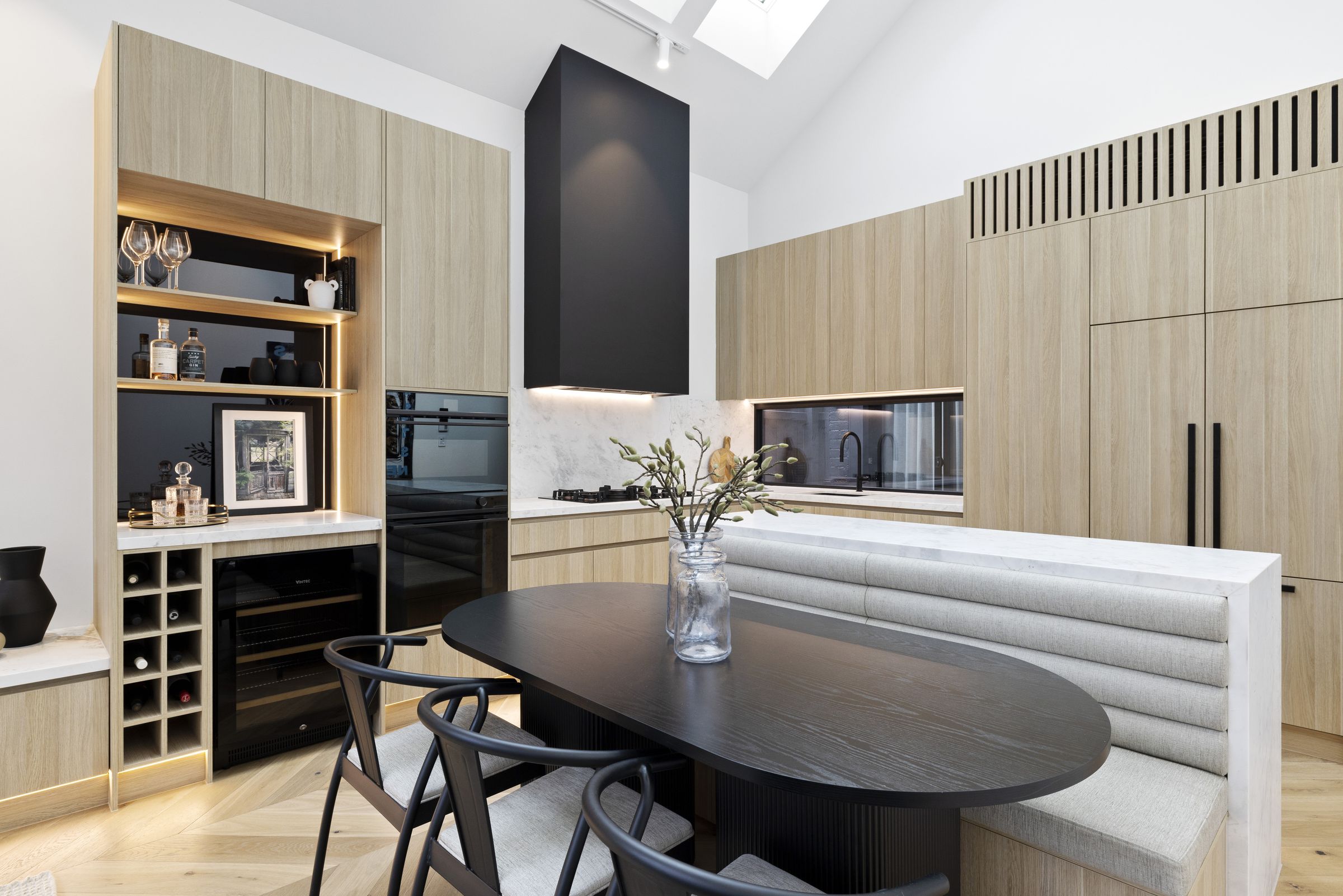 Banquette dining set into a marble-topped island, with a black rangehood and lit bar joinery behind