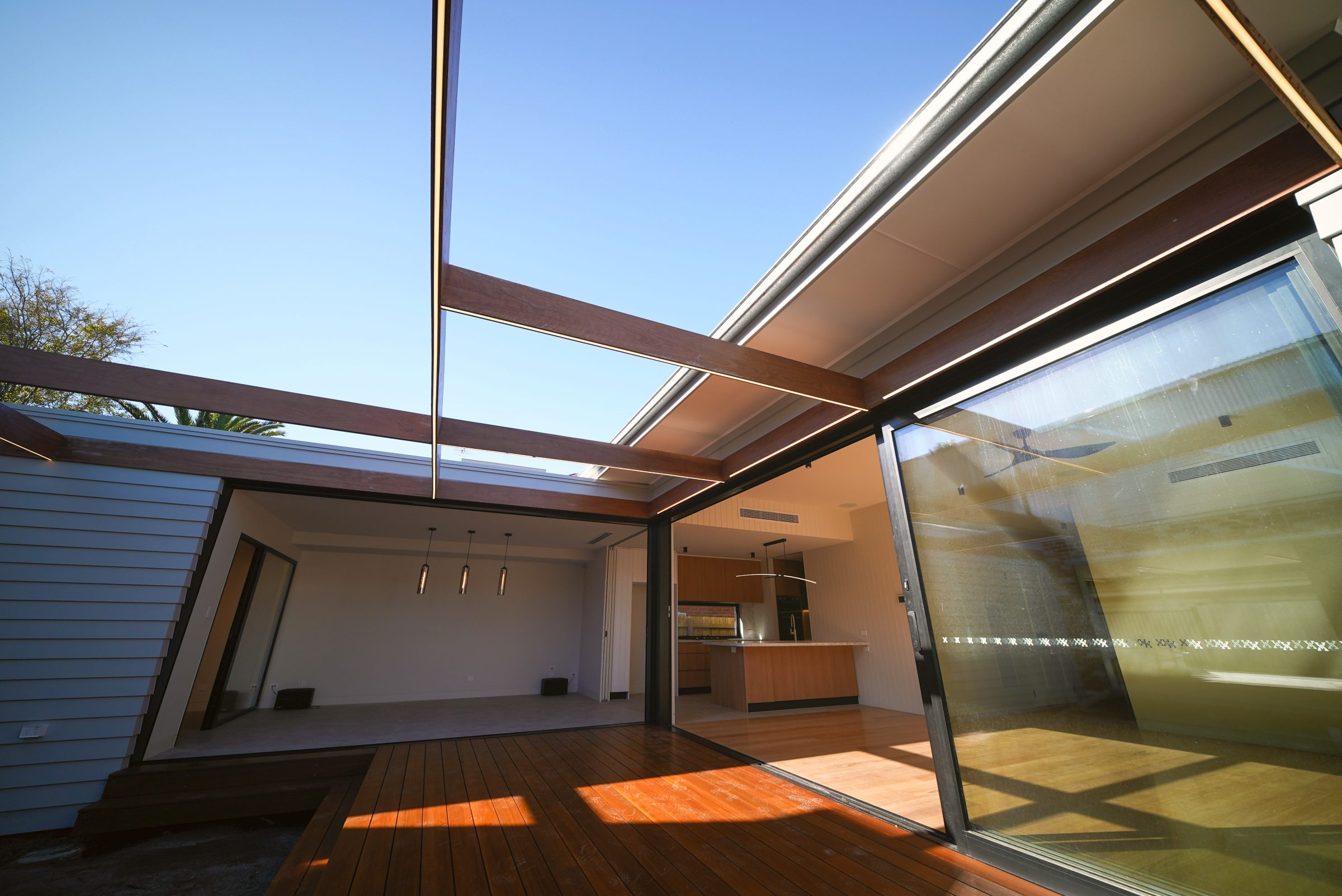 Looking up through the hardwood pergola beams to the sky, with the rumpus room and kitchen opening to the deck