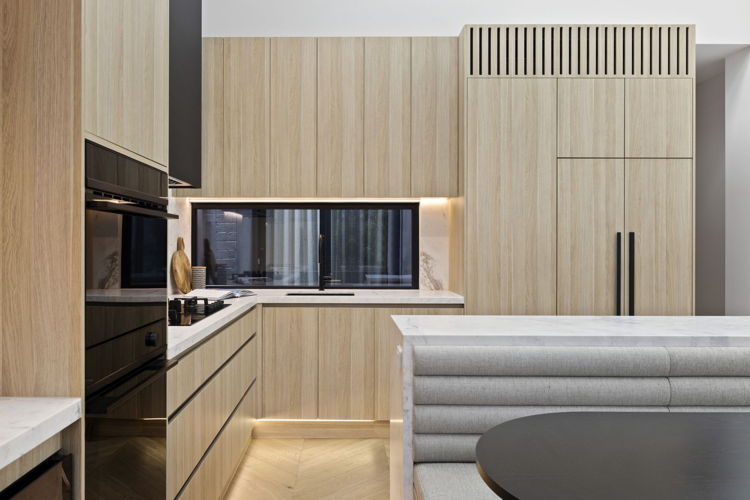 Lit bar shelving with a marble benchtop beside black ovens and the kitchen run