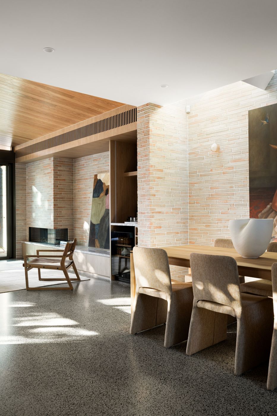 Dining table beneath a brick wall washed by skylight