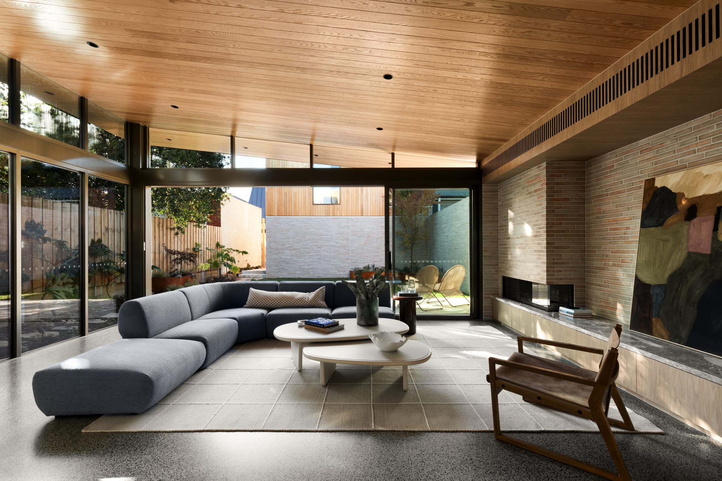 Living room at Balston, with a timber-lined ceiling, brick fireplace wall and full-height glazing opening to the garden